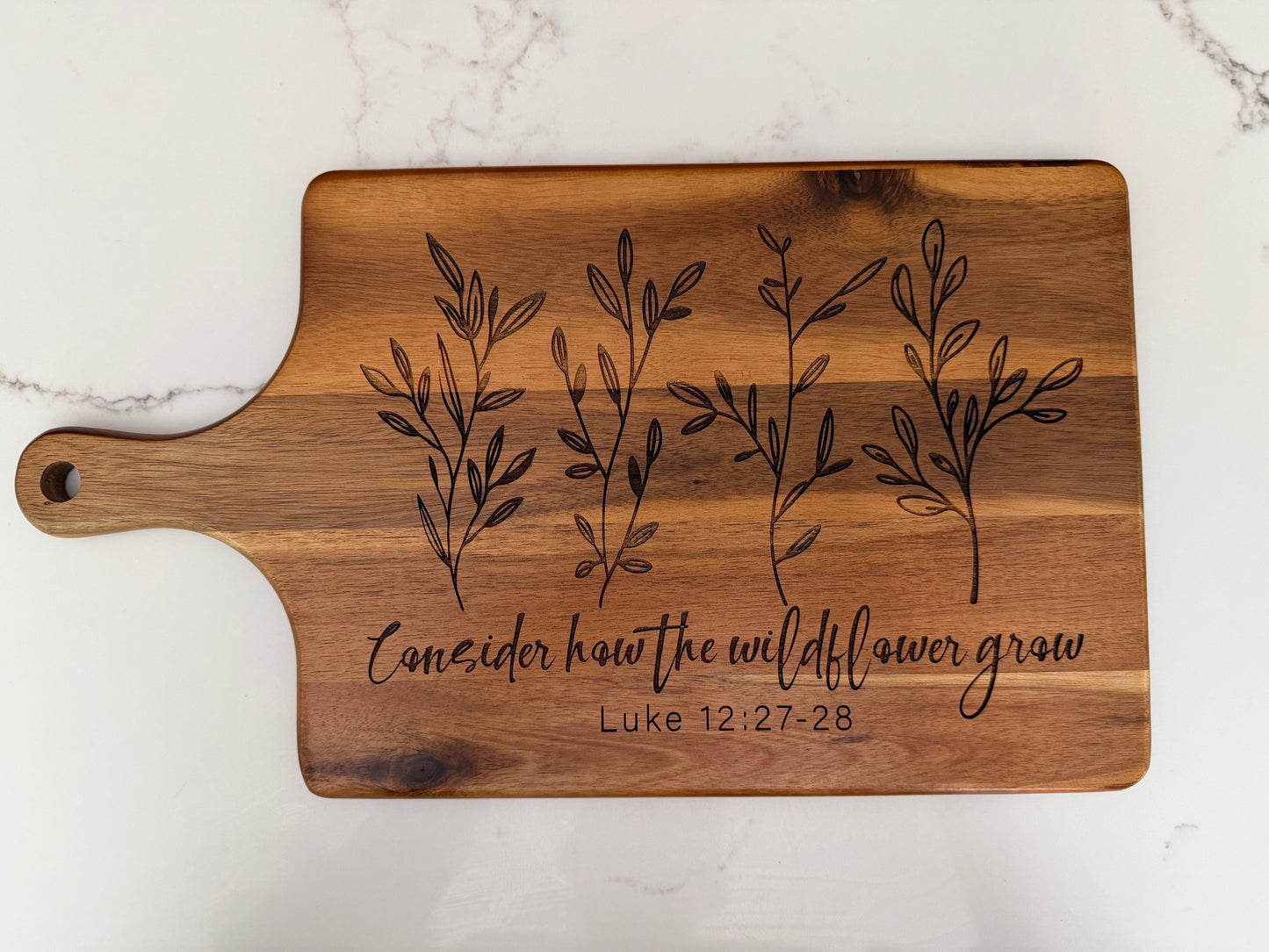 Faith inspired engraved acacia wood cutting board with scripture Luke 12:27-28, rustic Christian kitchen decor by Sons & Daughters.